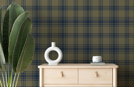 A cozy room features a dark olive green and navy blue plaid wallpaper.
The detailed design shows intersecting dark stripes over a muted green base.
In front, a light wood chest of drawers stands next to a small matching side table.
The rustic space is accented with large potted plants and minimalist wall shelves.