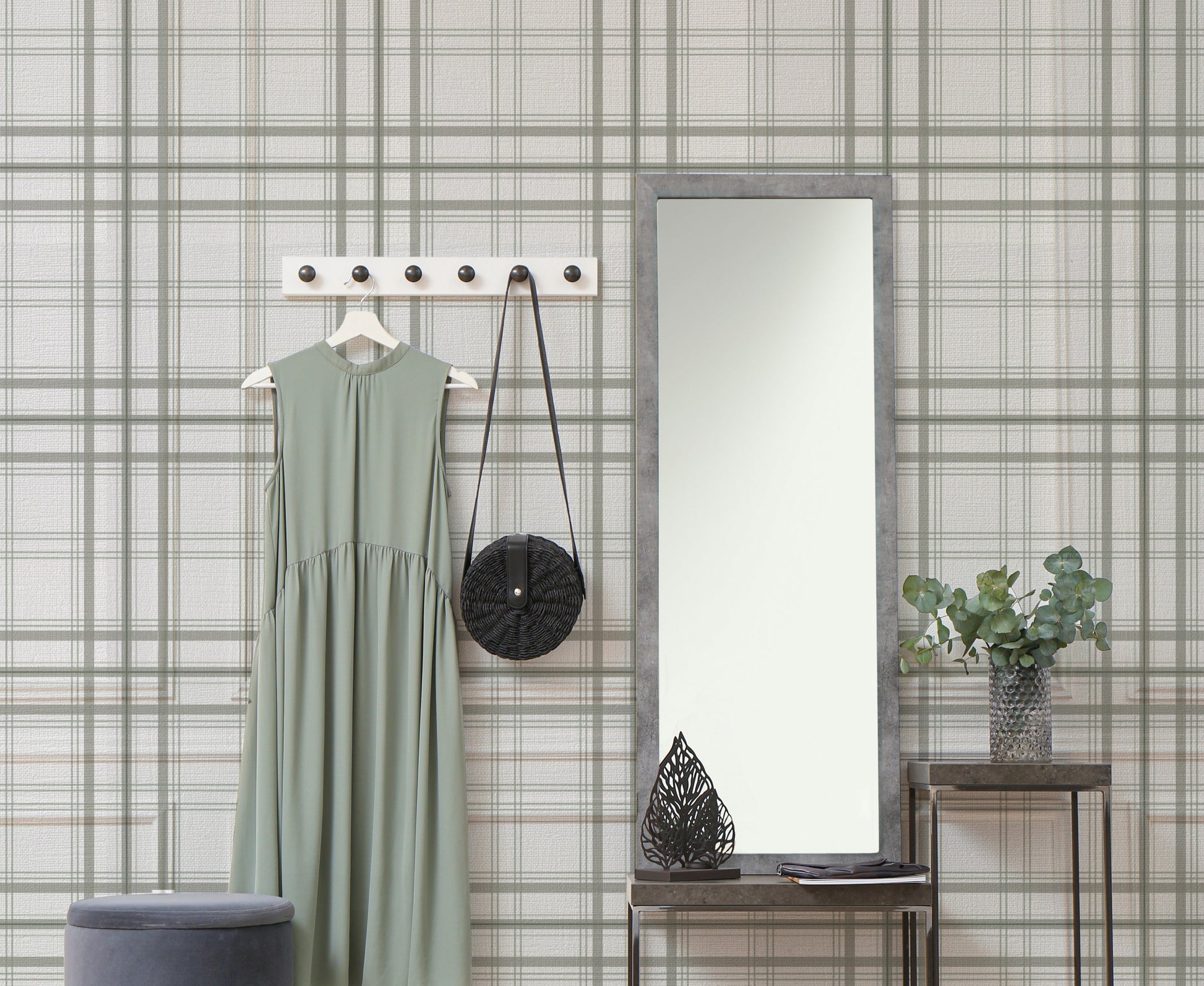 A warm interior setup features a soft faded olive green and grey plaid wallpaper.
The detailed design shows thin dark lines intersecting to form clean grids across a light olive base.
In front, a light wood media console with woven rattan doors is centered nicely.
The relaxing space is accented with a wooden armchair, decorative pottery, and dried botanical stalks.