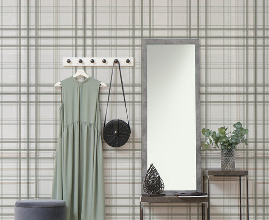 A warm interior setup features a soft faded olive green and grey plaid wallpaper.
The detailed design shows thin dark lines intersecting to form clean grids across a light olive base.
In front, a light wood media console with woven rattan doors is centered nicely.
The relaxing space is accented with a wooden armchair, decorative pottery, and dried botanical stalks.
