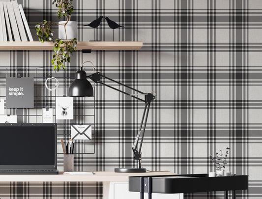 A modern home office features a classic charcoal grey and off-white plaid wallpaper.
The detailed pattern shows intersecting dark lines creating a clean grid on a light base.
In front, a sleek white study desk setup holds a laptop, lamp, and floating bookshelf.
The organized workspace is complete with a black office chair and a rolling utility cart.