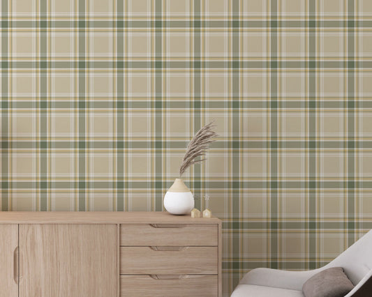 A modern living space featuring a muted wheat-beige, sage green, and white plaid wallpaper accent wall. In the center, a light oak sideboard cabinet with wooden legs holds a small wooden tripod lamp, a geometric candle, and a round white ceramic vase with a single sprig of dried pampas grass. To the left, a woven basket sits on the light wood floor, filled with tall, fluffy pampas grass stalks and a draped blanket.