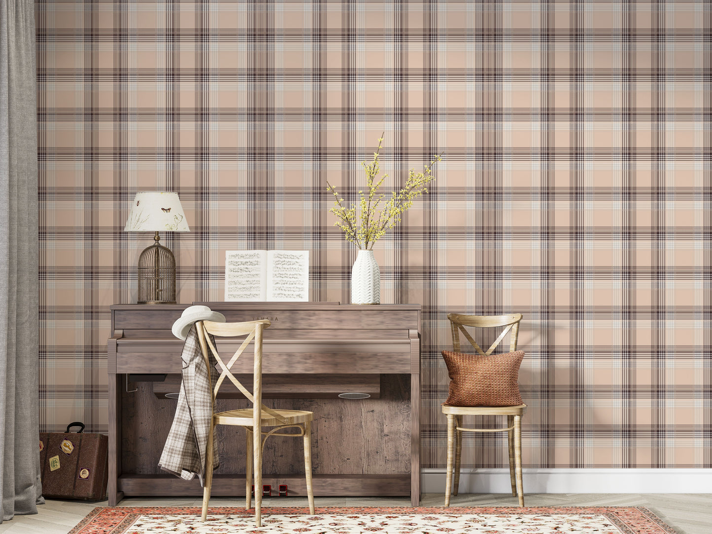 A closeup of a cozy interior setting featuring a dusty rose-pink and brown plaid wallpaper. On the left, a textured white ceramic vase with yellow flowering branches sits on top of a weathered, dark wood console table or upright piano. Next to it, a light wood cross-back dining chair holds a textured, rust-orange accent pillow.