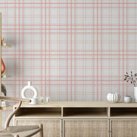 A calm living area features a textured, soft rosy haze pink and white plaid wallpaper.
The detailed design shows thin coral-pink lines intersecting to form clean grids across a light base.
In front, a light wood media console with woven rattan doors is centered nicely.
The relaxing space is accented with a wooden armchair, decorative pottery, and dried botanical stalks.