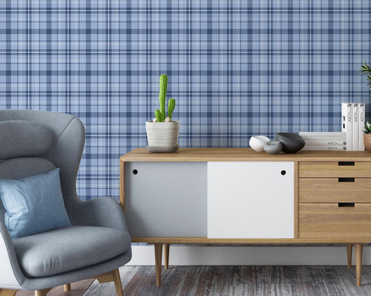 A contemporary living room with blue plaid wallpaper creating a textured backdrop. The space features a gray upholstered armchair, a mid-century modern wooden sideboard with decorative objects and books, and a large potted indoor tree on dark wood flooring.