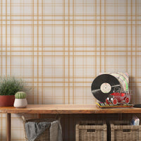 A stylish living area features a warm golden yellow and white plaid wallpaper.
The detailed design shows thin white lines intersecting to form clean grids across a yellow base.
In front, a cream-colored wooden sideboard with woven rattan doors is centered nicely.
The bright setup is accented with a white desk lamp, pottery, and a leafy green plant.