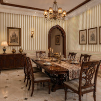 Traditional dining room featuring heritage-inspired cream and blush striped wallpaper with an ornate floral border, carved wooden dining table and chairs, vintage chandelier, classic artwork, and elegant Indian-inspired architectural details creating a warm and luxurious ambiance.