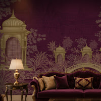 A luxurious living room scene featuring a deep purple velvet sofa with decorative pillows, set against a matching purple wall with a detailed white and gold architectural mural of domes and bridges. A gold table lamp sits on a dark wood side table next to the sofa.