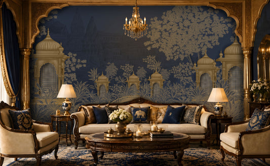 Luxurious living room featuring a royal Indian-inspired interior with a large navy blue and antique gold mural depicting domed pavilions, lush trees, and intricate architectural motifs. The space includes an ivory upholstered sofa, matching armchairs, carved dark wood furniture, navy and gold accent cushions, warm table lamps, a crystal chandelier, a round wooden coffee table with candles and flowers, and an ornate blue patterned rug, creating an elegant and opulent atmosphere.