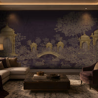 Contemporary luxury living room featuring a heritage-inspired mural in deep royal plum and antique gold. The mural depicts ornate domed pavilions, lush botanical foliage, an elegant arched bridge, blooming lotus flowers, and graceful swans on a tranquil pond, with subtle palace architecture in the background. The room is furnished with a cream sectional sofa, a plush mauve accent chair, dark wood cabinetry, a marble-top coffee table, layered neutral textiles, and warm ambient lighting, creating a sophistica