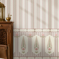 A styled interior room showing wallpaper with vertical pink and cream stripes and a decorative border along the lower portion. A wooden chair with a white embroidered pillow, a small wooden cabinet with a brass lantern, a bench, rug, and window are visible.