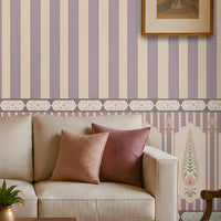 A styled living room featuring lavender and cream vertical striped wallpaper as the main product, shown in a complete interior setting with a beige sofa, wooden coffee table, patterned rug, and an armchair.