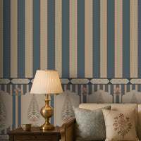 A styled interior scene showing a cream sofa with patterned pillows, a brass table lamp on a wooden side table, and a wall covered in blue and beige vertical striped wallpaper with a decorative border.
