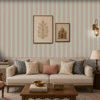 Elegant living room with a cream sofa and patterned blue, cream, and dusty-pink cushions, a carved wooden coffee table, cane armchair, decorative side tables, framed botanical and architectural artwork, brass lanterns, and pastel striped floral wallpaper.
