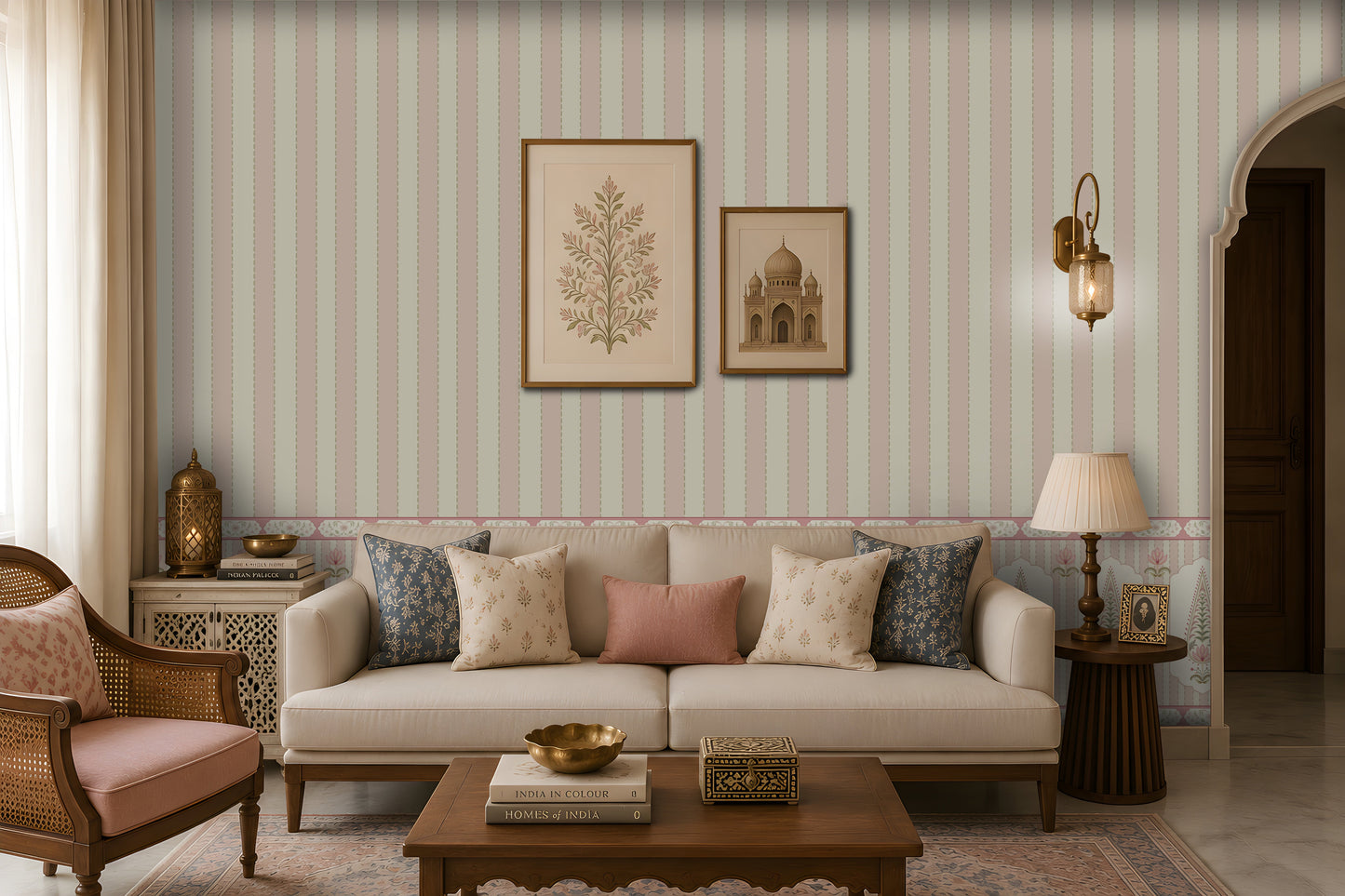 Elegant living room with a cream sofa and patterned blue, cream, and dusty-pink cushions, a carved wooden coffee table, cane armchair, decorative side tables, framed botanical and architectural artwork, brass lanterns, and pastel striped floral wallpaper.
