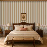 Warm, traditional bedroom featuring a carved dark-wood bed with cream bedding, a patterned coral accent pillow, matching bedside tables and lamps, a woven bench at the foot of the bed, striped and floral wallpaper, and tall curtained windows.
