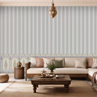 A styled living room featuring a prominent light blue and white vertical striped wallpaper with a decorative border along the bottom. The room is furnished with a cream-colored sectional sofa, wooden coffee table, and neutral-toned decor.