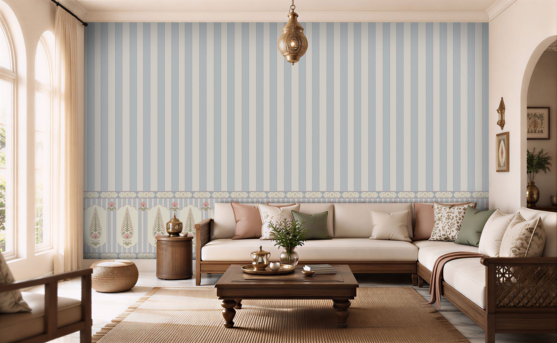 A styled living room featuring a prominent light blue and white vertical striped wallpaper with a decorative border along the bottom. The room is furnished with a cream-colored sectional sofa, wooden coffee table, and neutral-toned decor.
