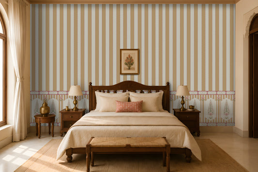 Warm, traditional bedroom featuring a carved dark-wood bed with cream bedding, a patterned coral accent pillow, matching bedside tables and lamps, a woven bench at the foot of the bed, striped and floral wallpaper, and tall curtained windows.
