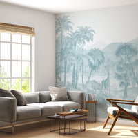 A vintage tropical wallpaper mural in a serene safari landscape is rendered in a monochromatic Cadet Blue color. The hand-drawn design features giraffes and deer amidst lush palm trees and mountains in an etched lithograph style. This nature-inspired, botanical accent wall creates a tranquil and sophisticated atmosphere in modern living spaces, pairing beautifully with grey textiles and natural wood furniture for a contemporary, bohemian-inspired look.