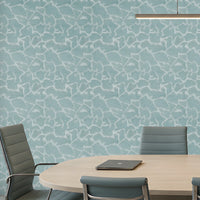 A modern conference room with a large oval wooden table, eight gray office chairs, a light blue patterned accent wall, and built-in shelving on the right side.