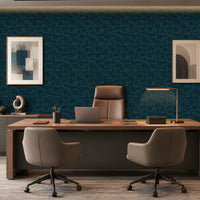 A modern office setup featuring a large wooden desk with two gray swivel chairs, a laptop, and a desk lamp, set against a dark blue patterned wallpaper wall with framed art.