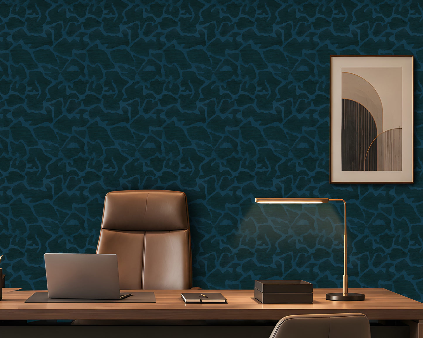 Dark teal patterned wallpaper in an office setting behind a wooden desk, a brown leather chair, a laptop, and a modern desk lamp, with a framed abstract print on the wall.
