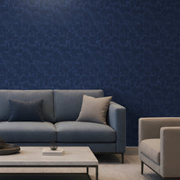 A modern living room setup featuring a prominent dark blue textured wallpaper on the back wall, a slate blue fabric sofa with two throw pillows, a light wood coffee table, and a light beige armchair.