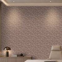 A modern office interior featuring a textured, abstract patterned wallpaper in dusty mauve and beige tones on the main wall. A light wood credenza with a black dome lamp and books sits on the left, and a beige leather office chair is on the right.