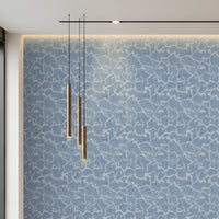 A modern interior wall featuring a blue and white abstract crackle pattern, with three hanging cylindrical pendant lights and a linear ceiling light above.