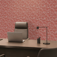 A modern home office setup featuring a large wooden desk, a gray leather executive chair, a silver laptop, a black desk lamp, and a pen cup, set against a distinctive pink and white abstract patterned wall.