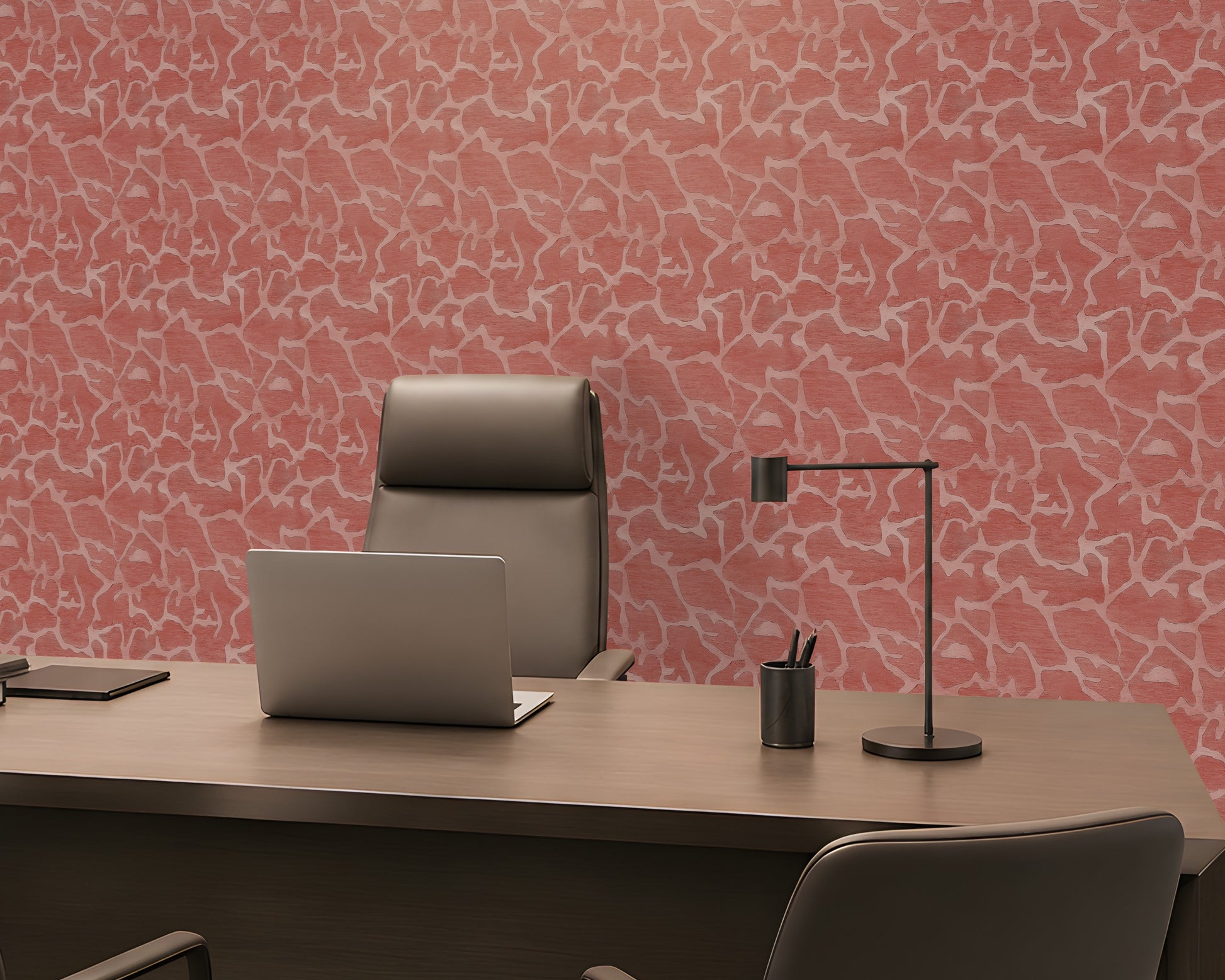 A modern home office setup featuring a large wooden desk, a gray leather executive chair, a silver laptop, a black desk lamp, and a pen cup, set against a distinctive pink and white abstract patterned wall.