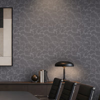 A styled interior room featuring textured gray wallpaper with a light organic crackle pattern, a dark wood credenza, a black table lamp, black office chairs, and a framed abstract art print.