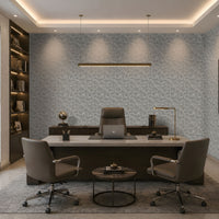 A modern office interior with a large desk, two gray office chairs, a round coffee table, built-in shelving, and patterned wallpaper on the back wall.
