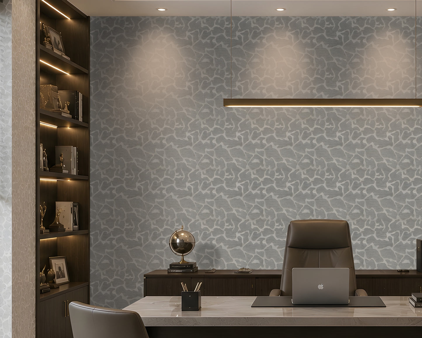 A modern home office featuring a light gray and white abstract patterned wallpaper on the main wall, a dark wood built-in bookshelf with warm lighting on the left, a white desk, a brown leather office chair, and a laptop on a desk mat.