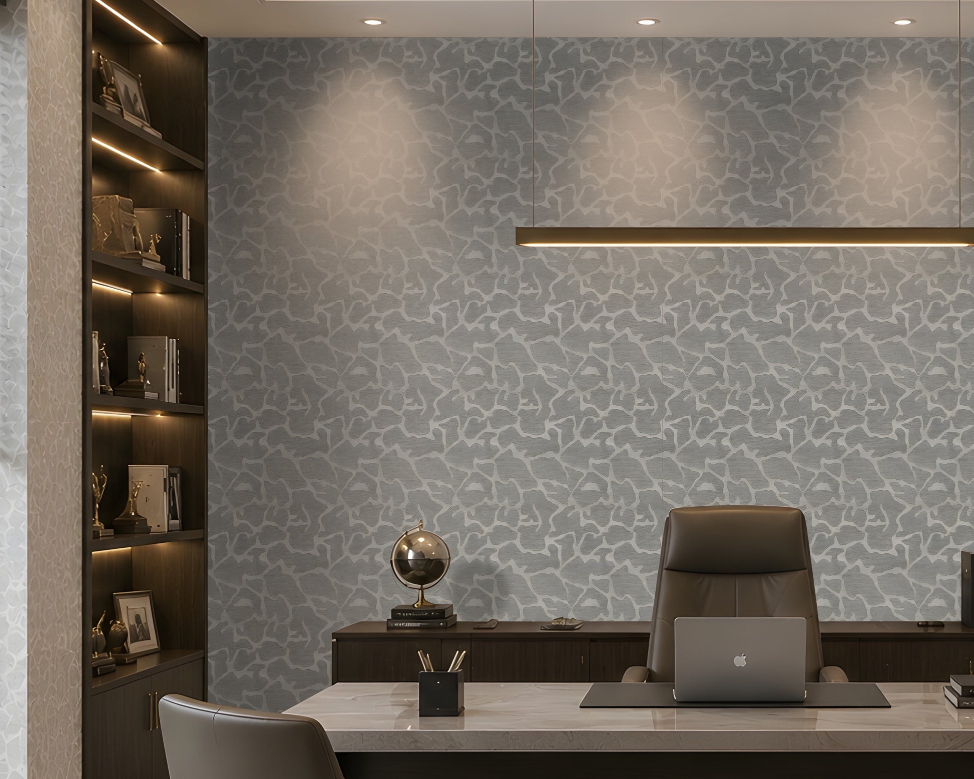 A modern home office featuring a light gray and white abstract patterned wallpaper on the main wall, a dark wood built-in bookshelf with warm lighting on the left, a white desk, a brown leather office chair, and a laptop on a desk mat.
