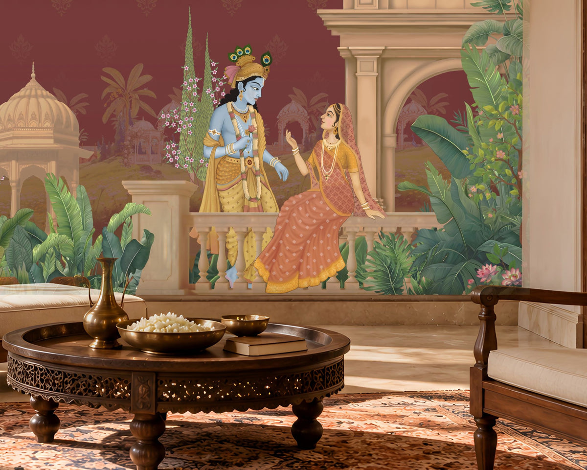 A large wall mural depicting the Hindu deity Krishna and the goddess Radha seated on a balcony, installed in a styled living room setting with a carved wooden coffee table and a wooden armchair in the foreground.