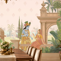 A styled dining room featuring a large wall mural with a classical Indian scene, including a peacock, pillars, and figures in traditional attire. The room is furnished with a wooden dining table, six upholstered chairs, a brass chandelier, and decorative plants.