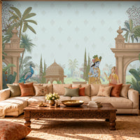 A styled living room featuring a large wall mural with a classical Indian scene, including a peacock, a woman in a blue sari, and architectural pillars, set behind a cream sectional sofa with decorative pillows.