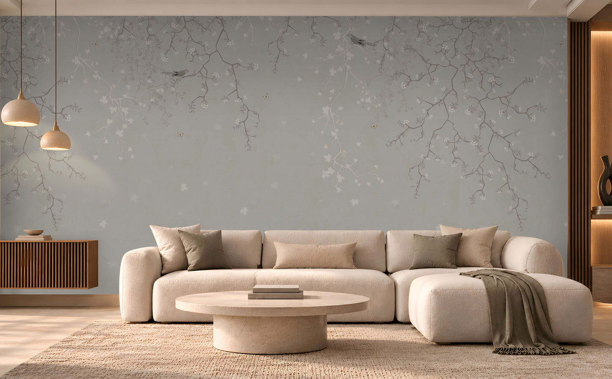 Modern luxury living room featuring Silent Breeze Mist Grey Botanical Birds Wallpaper with delicate branches, subtle floral motifs, a cream sectional sofa, minimalist coffee table, and warm ambient lighting.