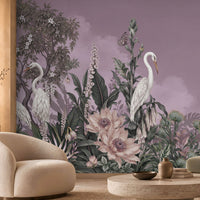 Whimsical mural featuring white herons amidst lush tropical flora dominates the back wall of a modern, neutral-toned living room. The mural displays a muted purple backdrop with a crescent moon, detailed green foliage, pale ivory blossoms, and tall trees.