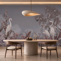 An elegant dining room featuring a large, scenic mural wallpaper illustration. The slate grey wallpaper depicts white herons standing amidst lush tropical foliage, flowering trees, and flying butterflies under a soft cloudy sky.