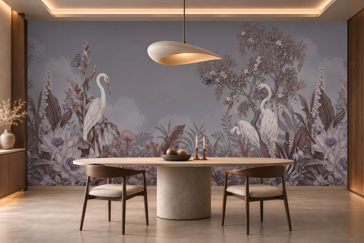 An elegant dining room featuring a large, scenic mural wallpaper illustration. The slate grey wallpaper depicts white herons standing amidst lush tropical foliage, flowering trees, and flying butterflies under a soft cloudy sky.
