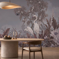 An elegant dining room featuring a large, scenic mural wallpaper illustration. The slate grey wallpaper depicts white herons standing amidst lush tropical foliage, flowering trees, and flying butterflies under a soft cloudy sky.