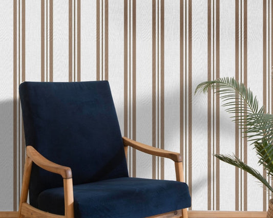 A bright seating area features a warm rustic mocha brown and white striped wallpaper.
The detailed design shows clean brown vertical lines repeating across a textured light base.
In front, a classic dark blue velvet armchair with a wooden frame sits comfortably.
The simple, inviting space is naturally accented with a leafy green potted plant nearby.