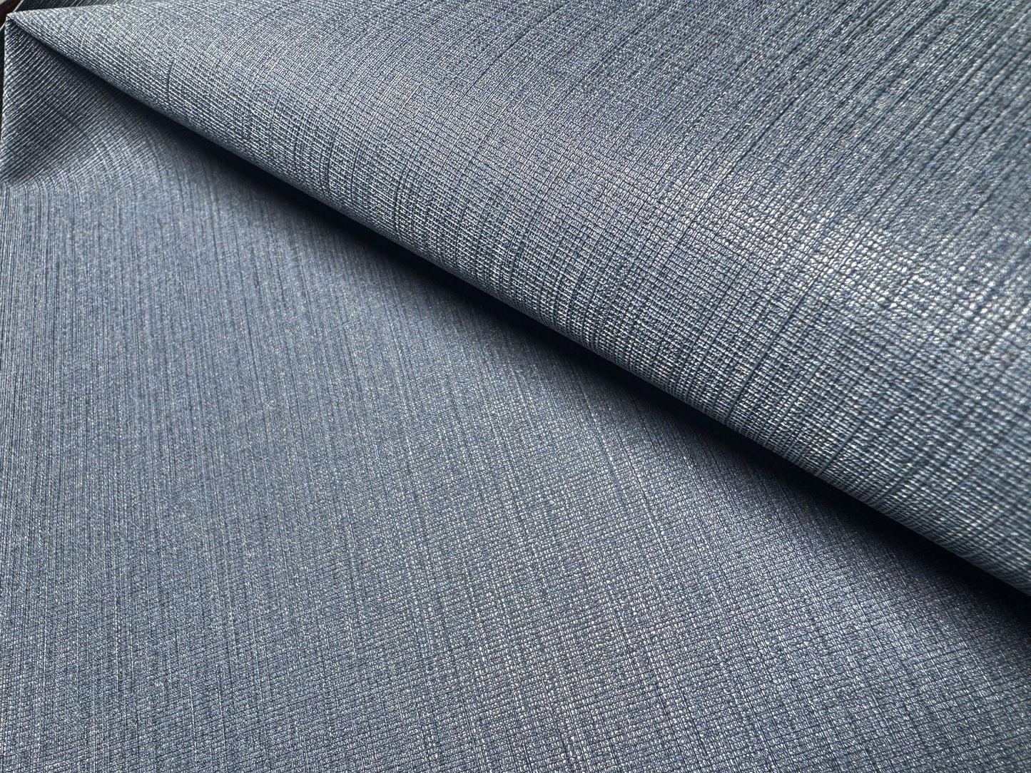 Close-up view of Waterproof Fabric Backed Commercial Wallcovering in Soft Steel Blue, showcasing a dense, industrial textile texture with a fine linear-weave pattern and a muted metallic blue and gray finish on a durable vinyl surface.