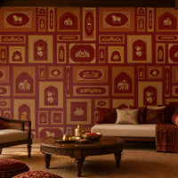The Royal Rajputana Courtyard wallpaper in Regal Wine Red featuring intricate Rajasthani palace-inspired motifs, elephant illustrations, floral artwork, Mughal arches, and antique gold detailing in a luxurious living room setting.