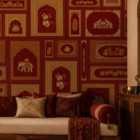 The Royal Rajputana Courtyard wallpaper in Regal Wine Red featuring intricate Rajasthani palace-inspired motifs, elephant illustrations, floral artwork, Mughal arches, and antique gold detailing in a luxurious living room setting.