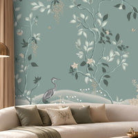 Timeless Avian Garden Mural in Misty Blue featuring delicate botanical branches, soft ivory flowers, graceful foliage, and elegant bird illustrations, creating a serene nature-inspired living room with a sophisticated misty blue and neutral colour palette, curved furniture, warm lighting, and contemporary décor.
