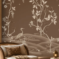 Warm brown botanical wallpaper mural featuring delicate ivory vines, leaves, blossoms, and elegant birds, styled in a luxurious living room with natural wood furniture, a cane accent chair, soft neutral seating, a textured rug, warm ambient lighting, and refined earthy décor.
