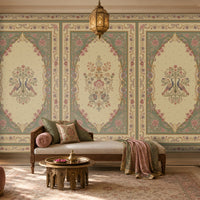 Vanamala Garden Mural Wallpaper - Antique Olive Green featuring elegant peacock motifs, floral bouquets, and ornate heritage-inspired frames in soft dusky teal blue and ivory tones, showcased in a luxurious Indian living room with carved wooden furniture, warm lighting, and classic decorative accents.